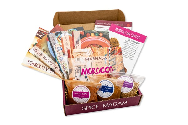 An open food subscription box labeled Spice Madam that is filled with 3 bags of spices and lots of recipe cards.