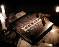 A Finders Seekers Escape Room Game subscription box with a magnifying glass on top and lit candles nearby.