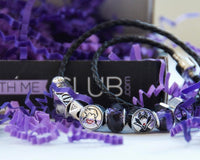 A Charm With Me Club subscription box filled with purple crinkle paper and a bracelet with several charms on it.