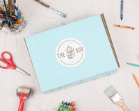 Outside the Box Creation's kids art box in its signature light blue color surrounded by art supplies on a flat surface